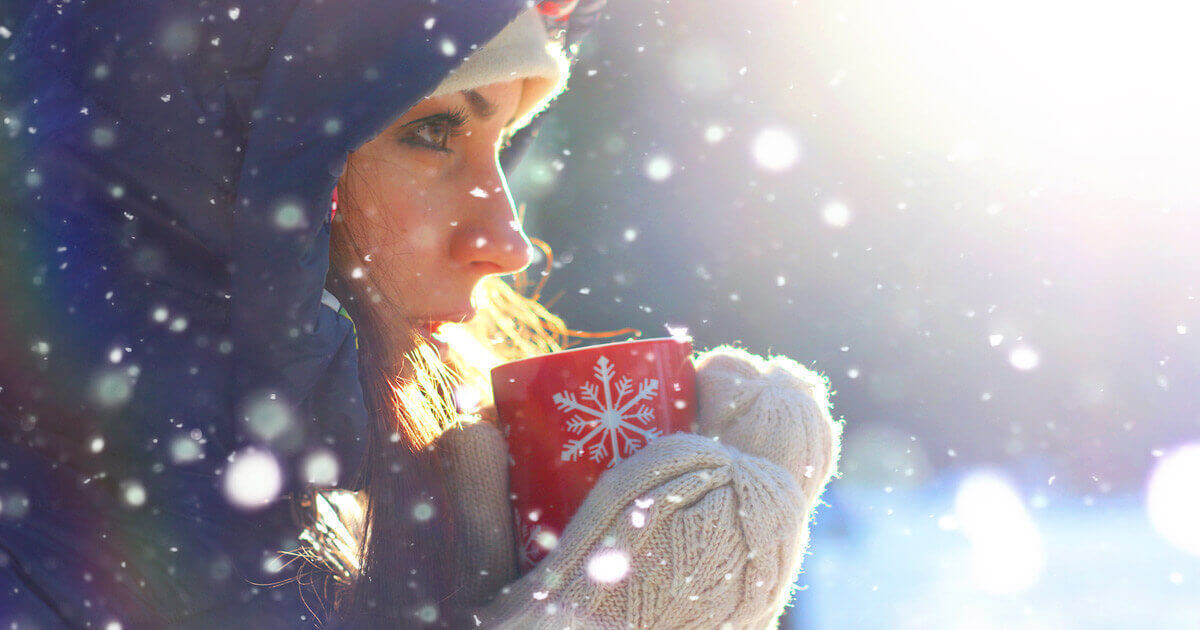 7 Effective Ways to Beat Holiday Stress Woman in a winter hood holding a warm mug in the snow